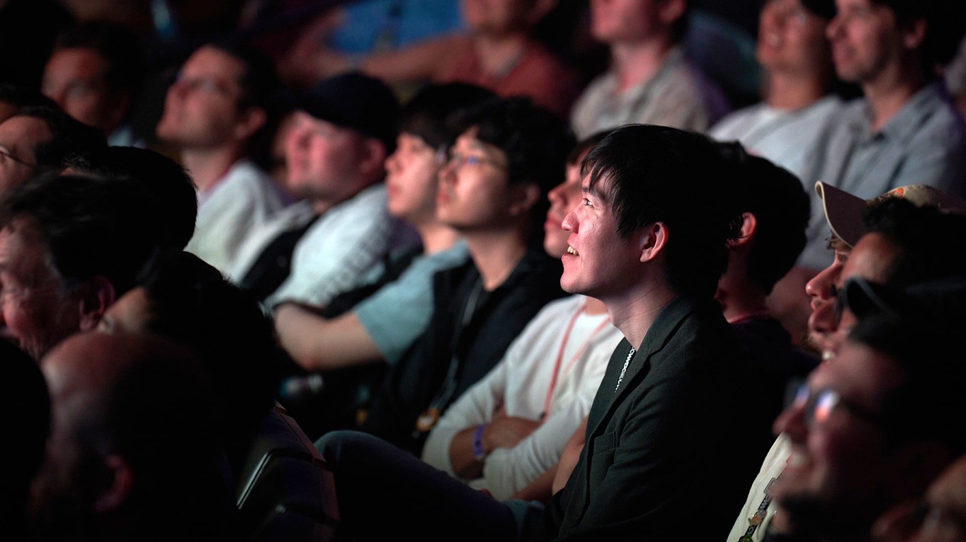 Members of an audience sit in a theater looking at a presentation on stage.